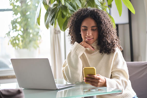 Person sitting at glass table with laptop while looking at their phone