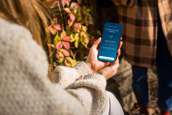 Person holding a smartphone showing the app to pay app with flowers in the background