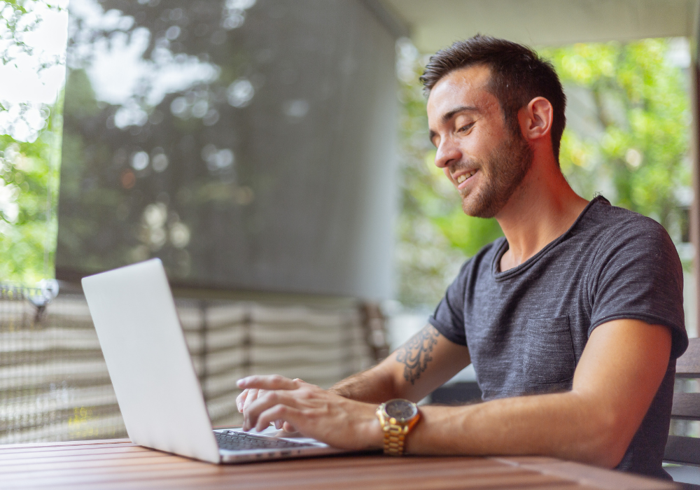 Man sat at a table looking at a laptop and smiling